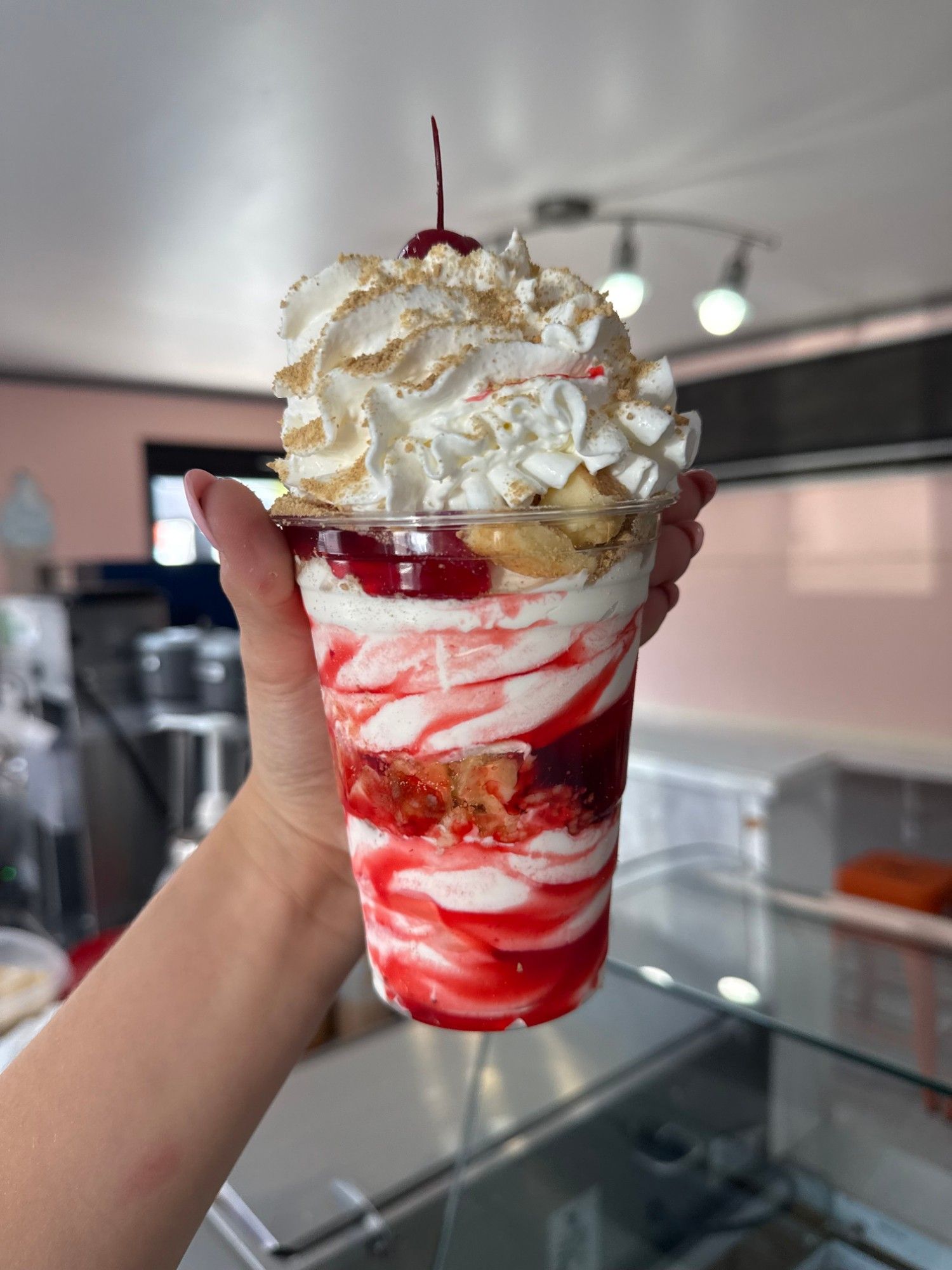 A tall cherry sundae layered with soft serve and cherry topping, crowned with whipped cream, graham crumbs and a cherry