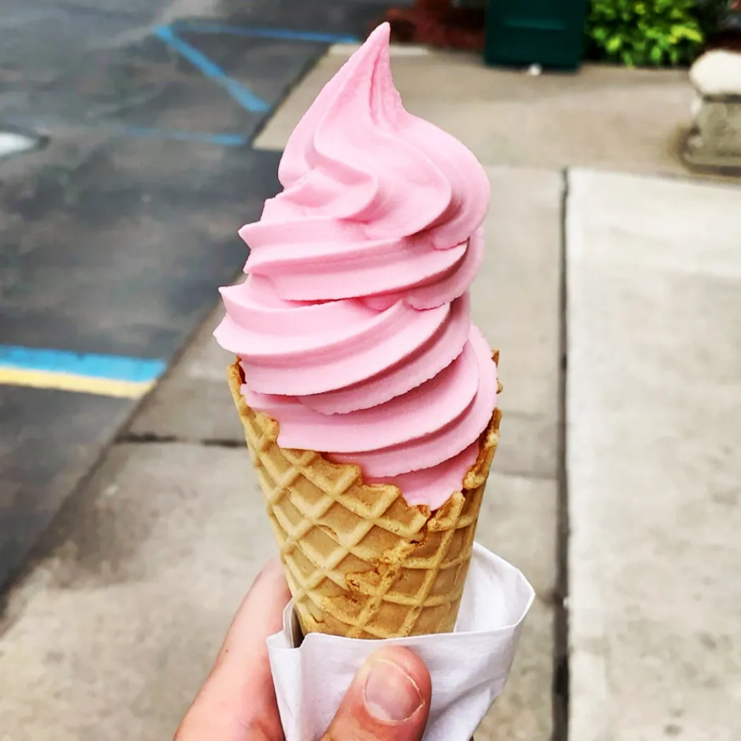 A pink soft serve cone dipped in chocolate sprinkles