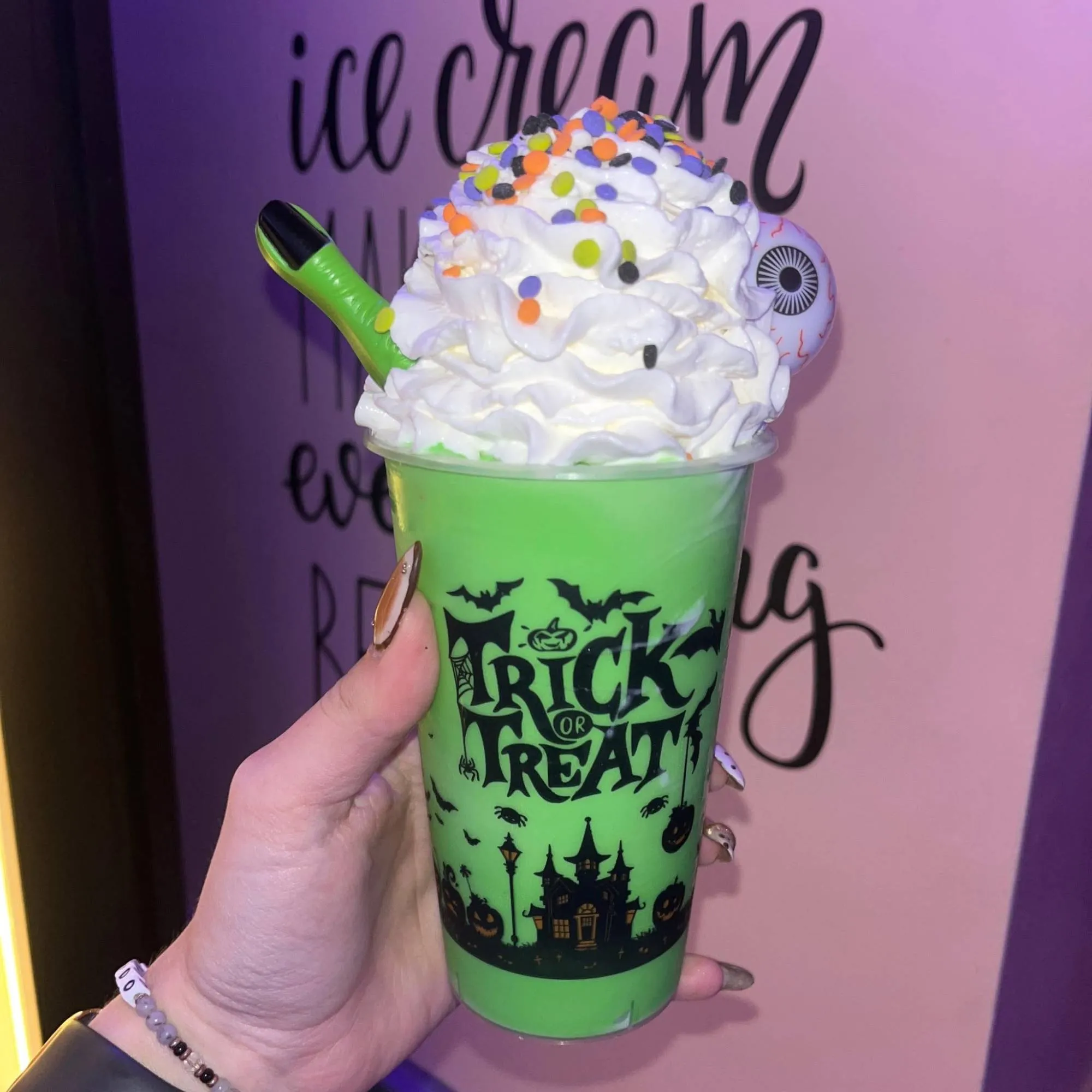 A green Halloween shake in a trick-or-treat cup with an eyeball and witch finger